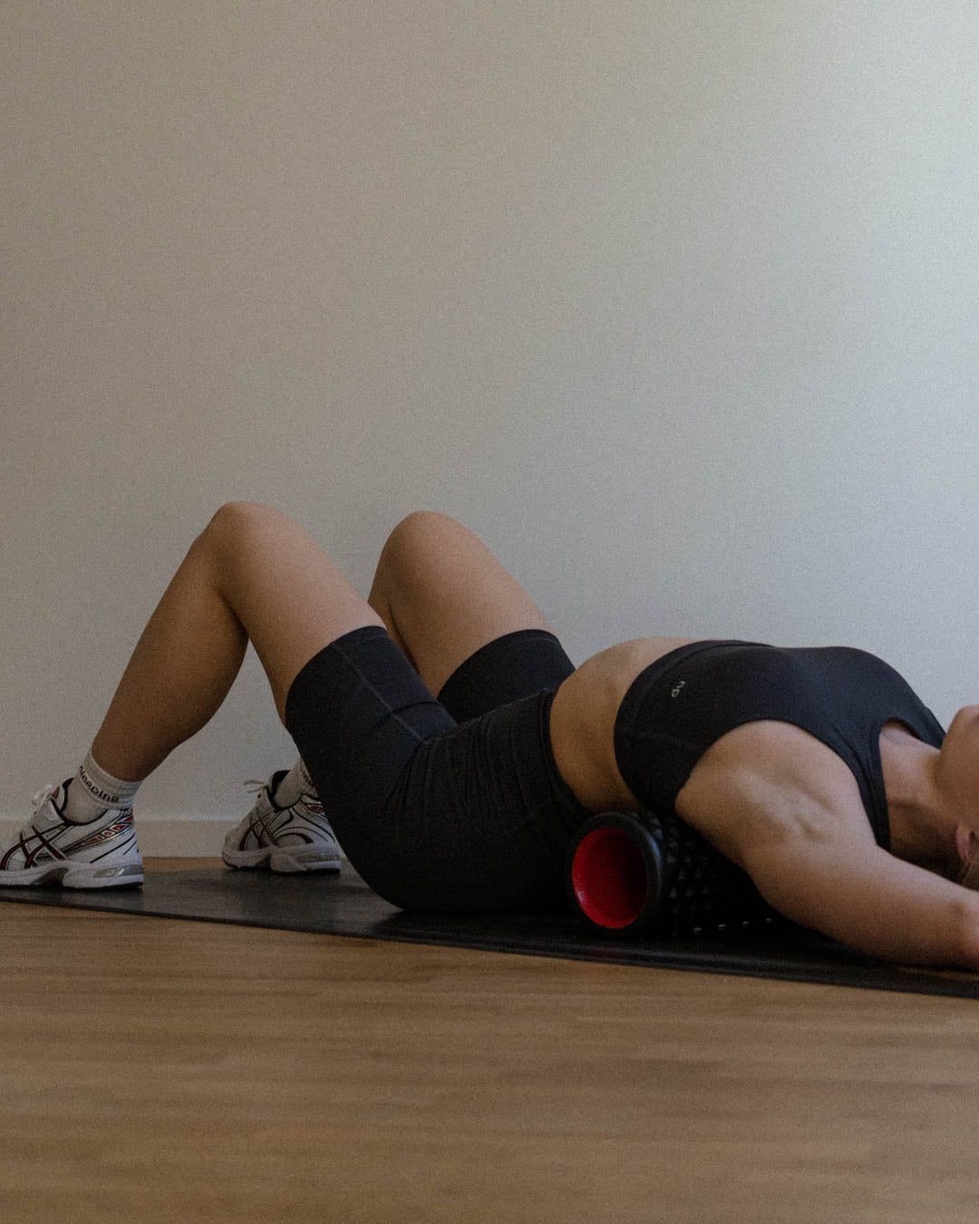 Woman in Ninepine sports bra and biker shorts lying on a foam roller on her back on a yoga mat