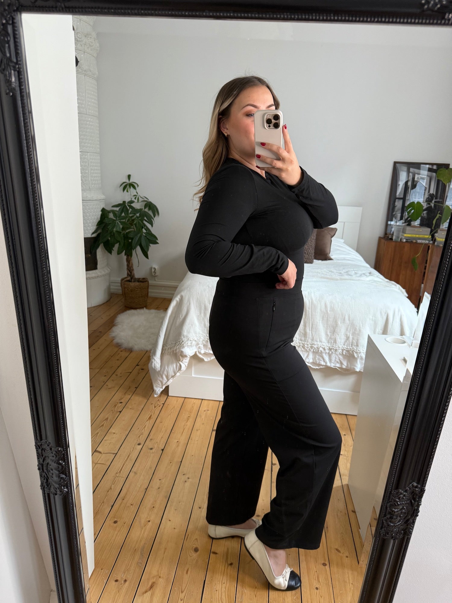 Curvy woman taking a mirror selfie in black Ninepine Asana Relaxed Trousers and a matching long-sleeve soft top, styled with two-tone flats for a clean, modern everyday outfit