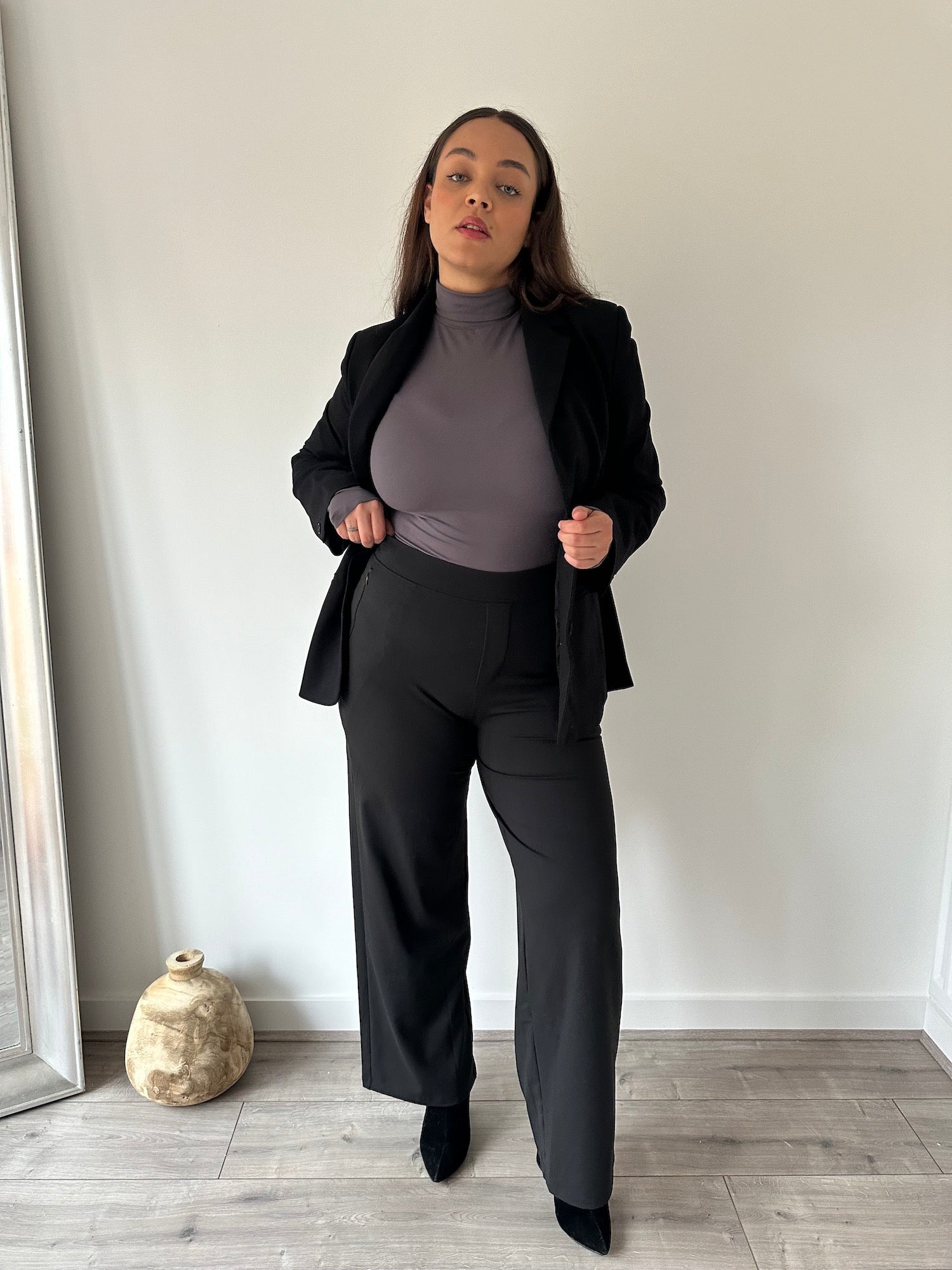 Curvy woman in black Ninepine Asana Relaxed Trousers, charcoal soft turtleneck, and Perfect Blazer, showcasing a comfortable, tailored outfit for everyday and office wear