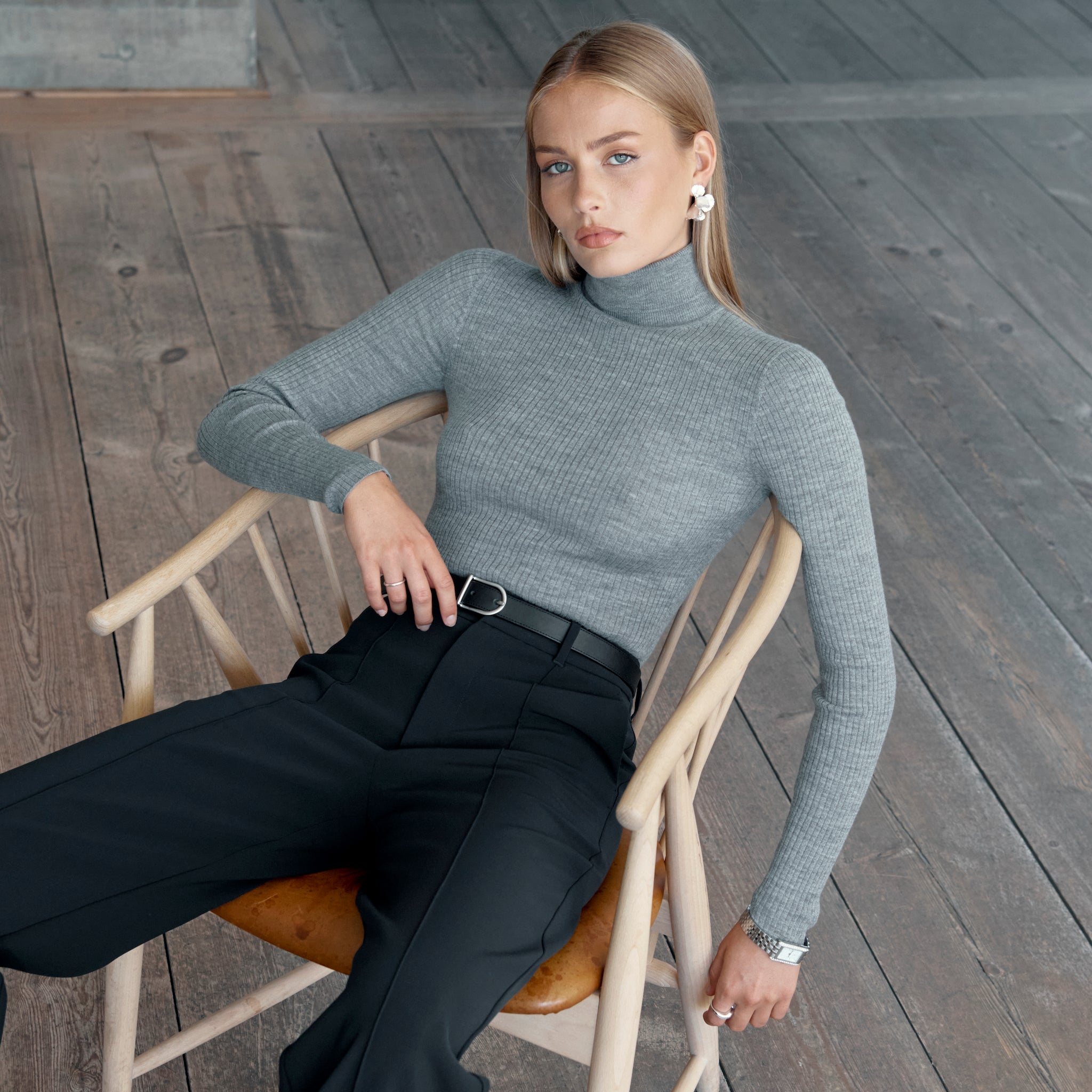 Woman sitting in chair wearing black Ninepine Crepe Relaxed trousers styled with a grey ribbed turtleneck and belt.